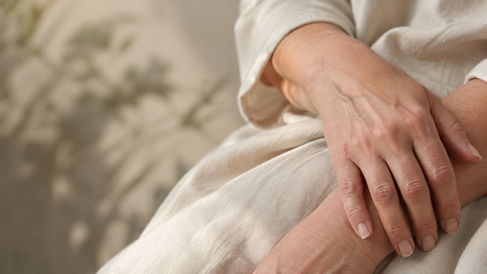 Mature woman's hands resting on cream fabric, showing the natural contours and skin of the back of her hand