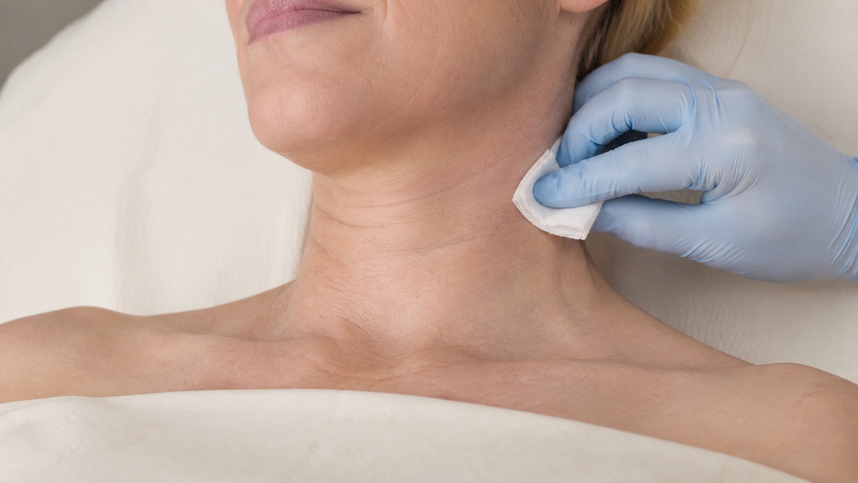 Close-up of neck skin being gently prepared with gauze by a gloved hand